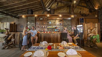 Una zona de bar rústica con vigas de madera, barra y estanterías con botellas.