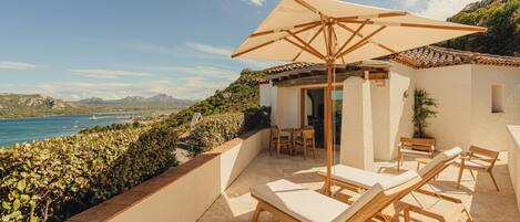 A sunlit patio with lounge chairs and a table, overlooking a coastal view.