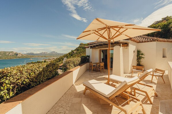 A sunlit patio with lounge chairs and a table, overlooking a coastal view. - Aethos Sardinia (Arzachena)