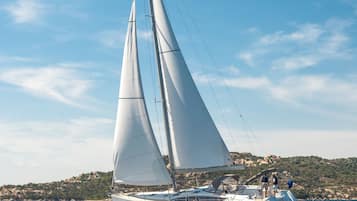 A sailboat with multiple sails on a calm sea, with a rocky coastline in the background.