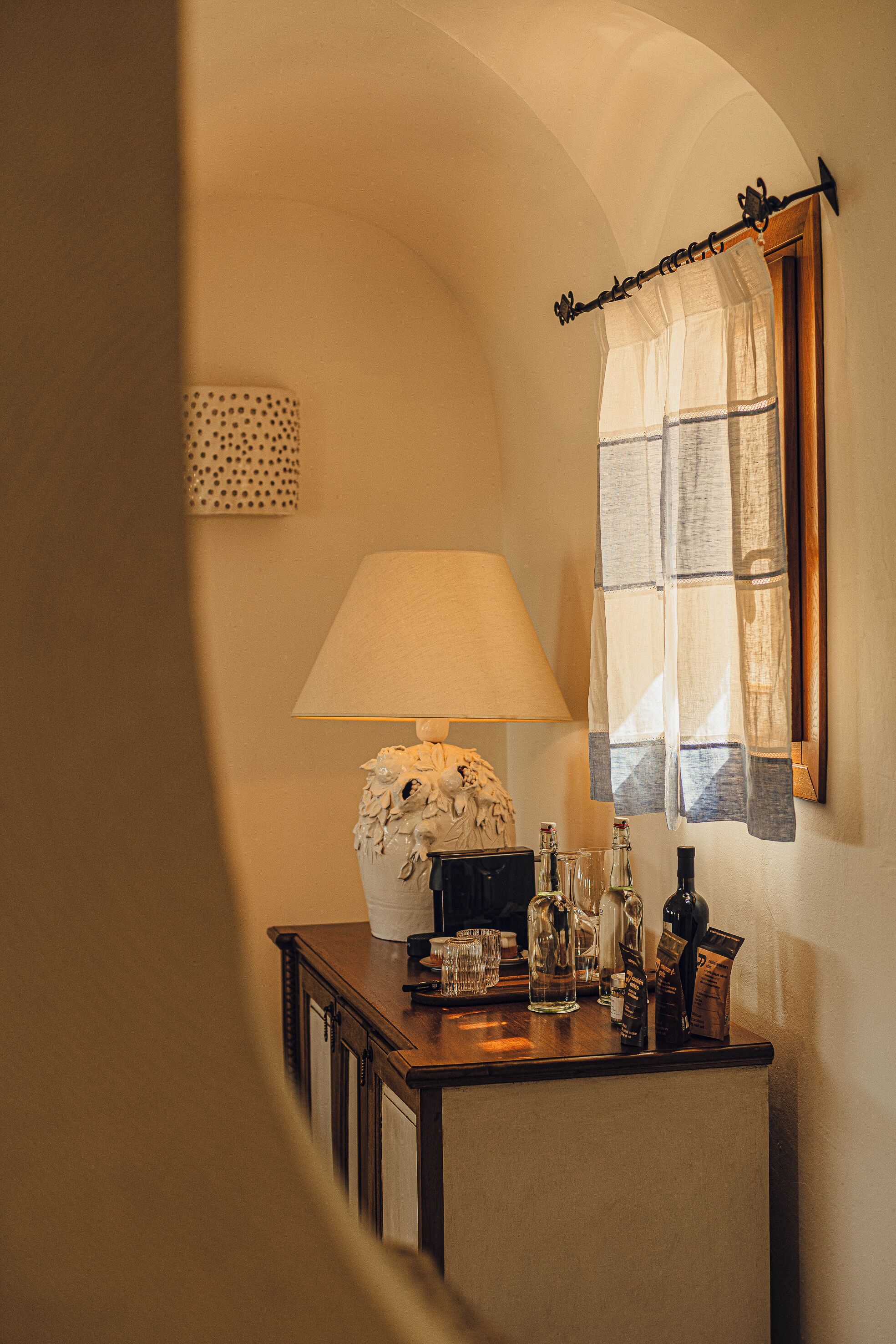 A corner of a room with a lamp, a mirror, and a window with curtains.