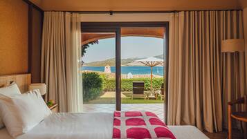 Ein Hotelzimmer mit Bett, Meerblick und einer Terrasse mit Stühlen und Sonnenschirmen.