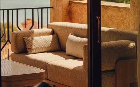 A balcony with a sofa and table, overlooking a body of water and hills.