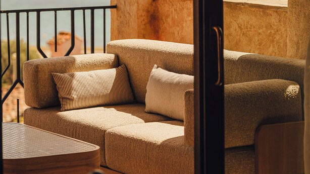 Un balcon avec un canapé et une table, donnant sur une étendue d’eau et des collines.