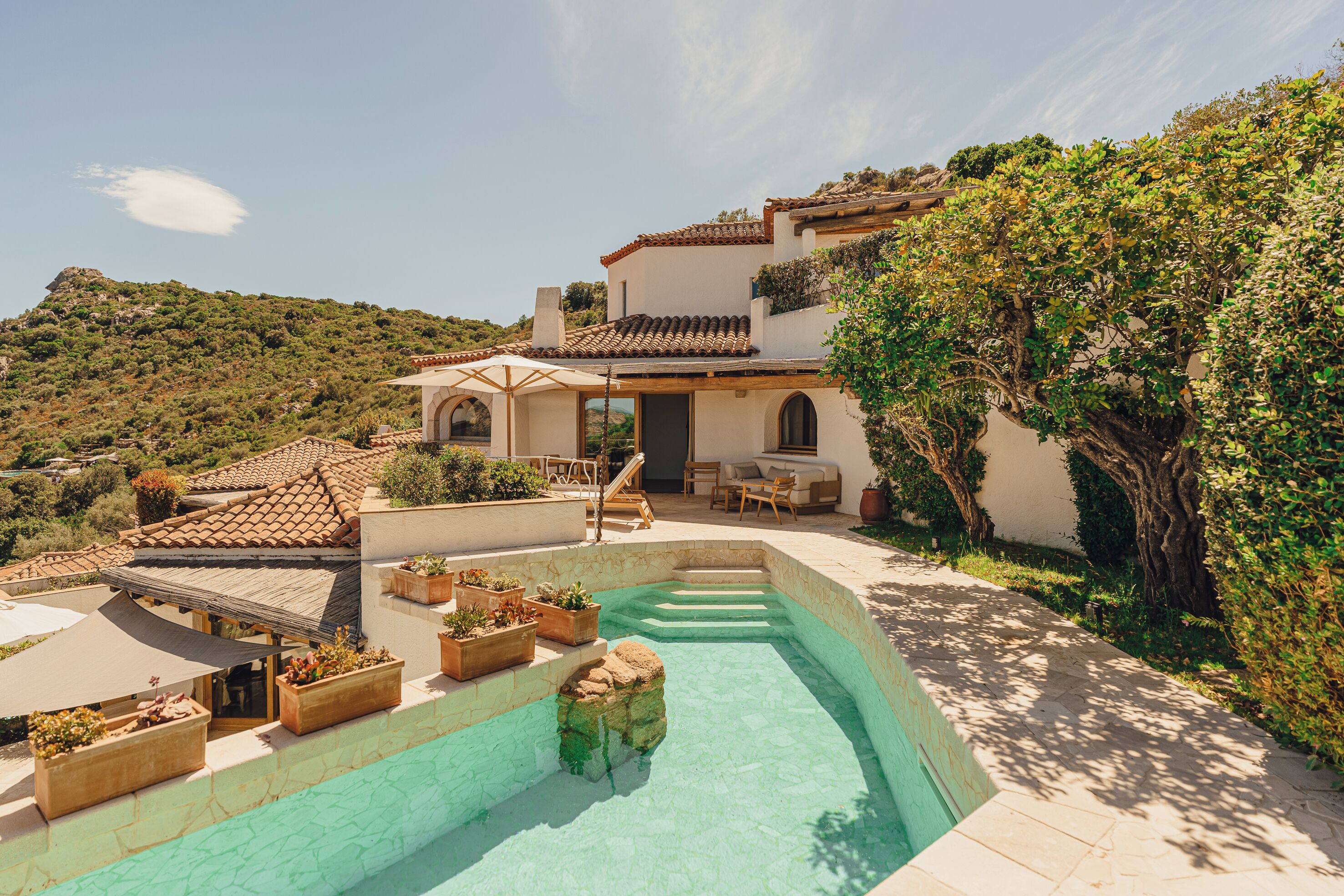 Un área de piscina con vistas despejadas del paisaje circundante, un patio con mobiliario exterior y un edificio con tejado de tejas.