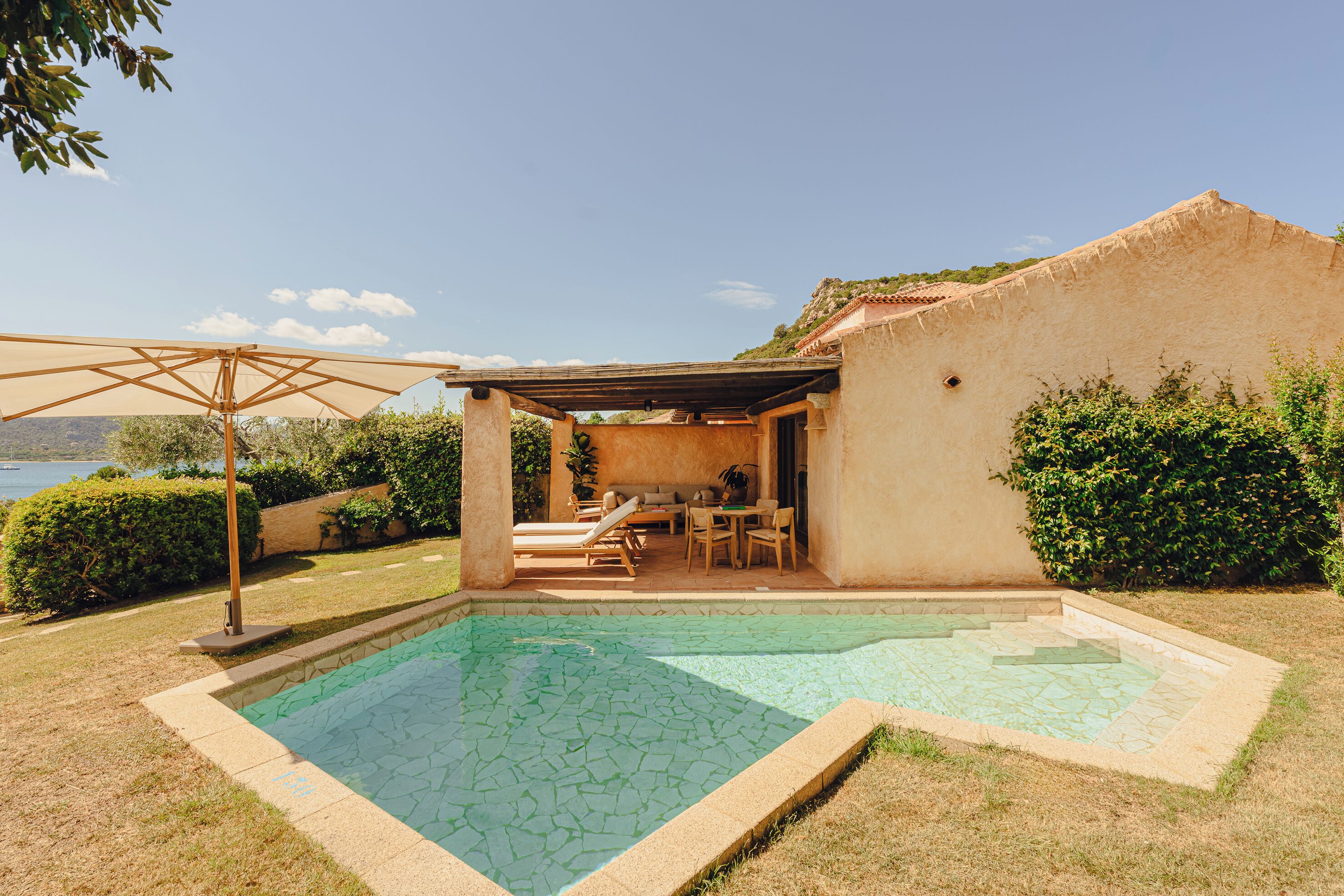 Une piscine avec une terrasse carrelée, un patio couvert avec des sièges et une vue sur la mer.