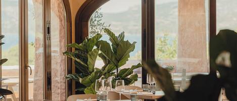 A restaurant with wooden tables and chairs, large windows, and hanging pendant lights.