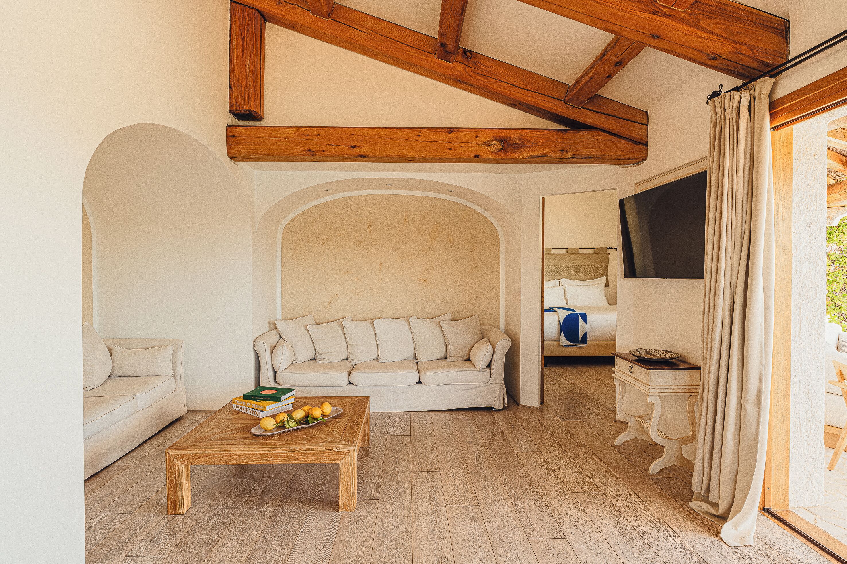 Una sala de estar con techo de madera, un sofá blanco, una mesa de centro con frutas y un televisor al fondo.