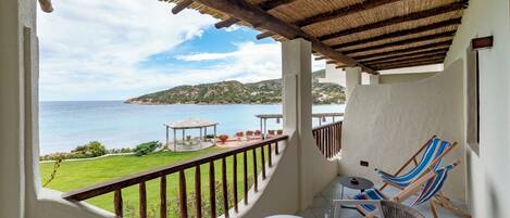 A balcony with a view of the sea, a table with chairs, and a small table with a vase.