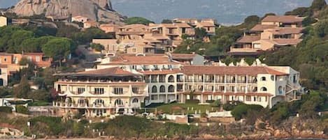 Un hotel costero con varias construcciones, una destacada formación rocosa al fondo y vista al mar.