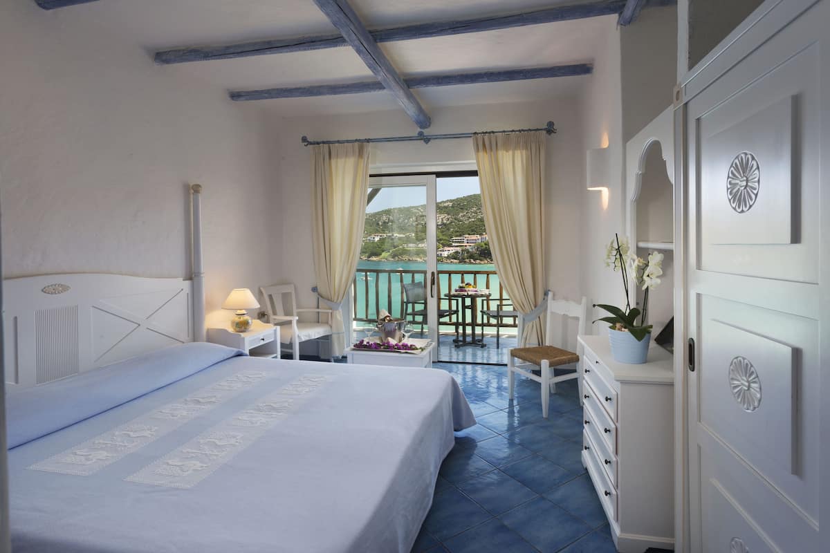 Een slaapkamer met een bed, een bureau, een stoel, een dressoir en een balkon met uitzicht op het landschap.