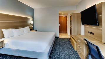A hotel room with a large bed, a desk with a chair, a flat-screen TV, and a wardrobe.