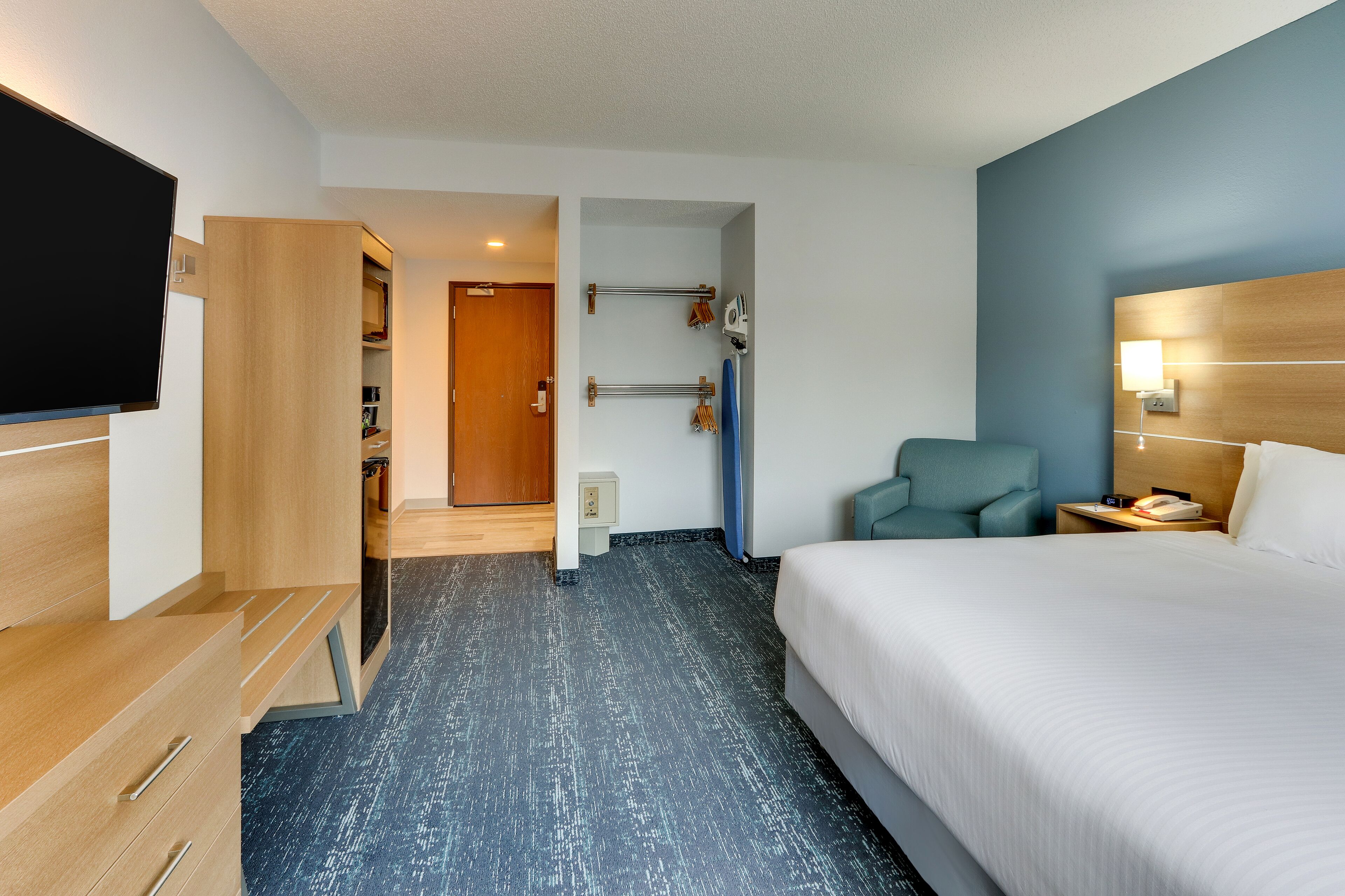 A hotel room with a bed, a TV, a desk, a chair, and a bathroom visible through an open door.