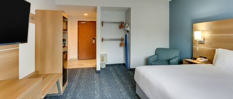 Ett hotellrum med en säng, en tv, ett skrivbord, en stol och ett badrum som syns genom en öppen dörr.