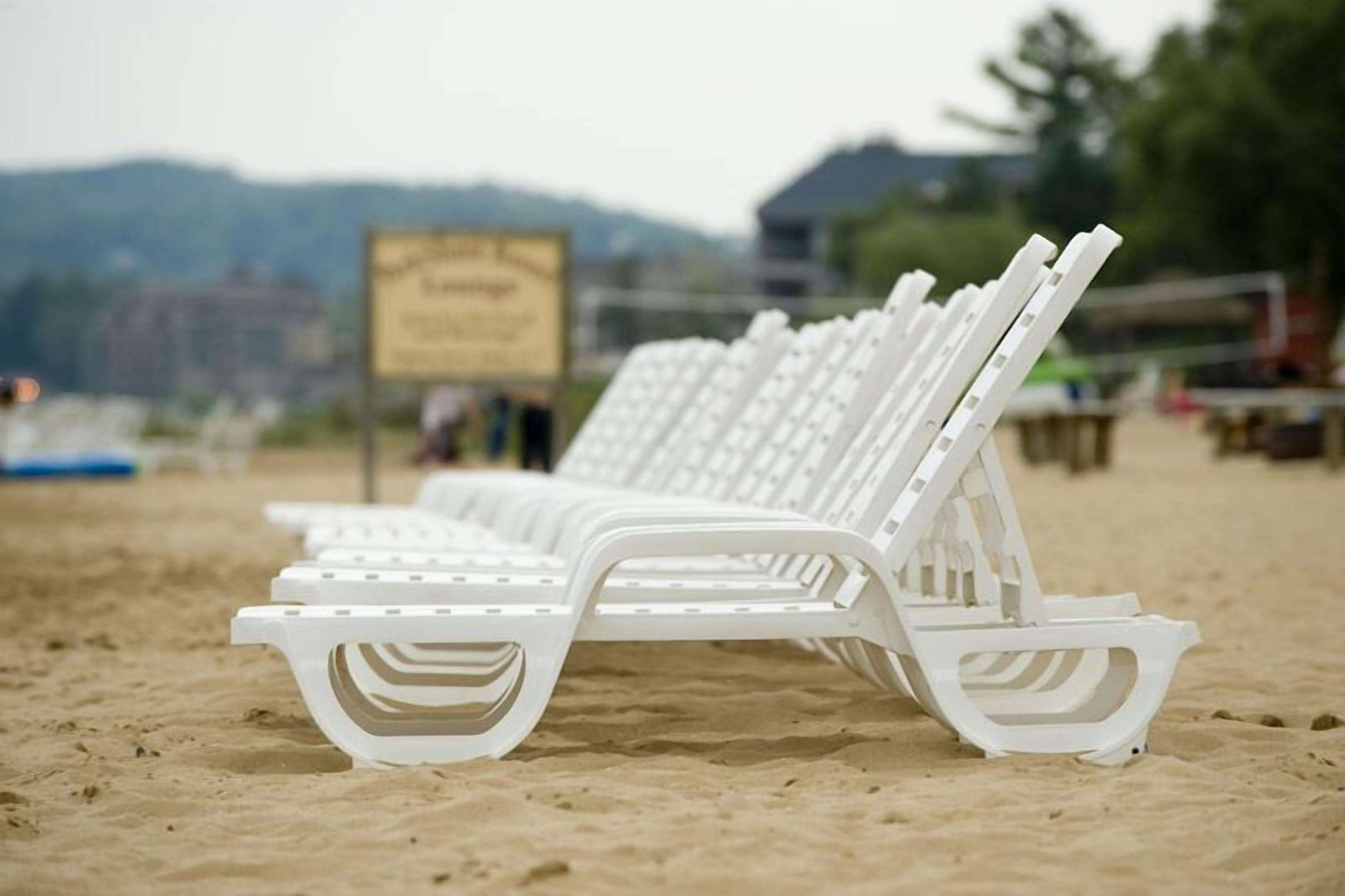 White beach chairs lined up on a sandy beach with a sign in the background.