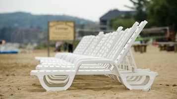 White beach chairs lined up on a sandy beach with a sign in the background.