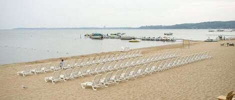 Una playa con hileras de sillas reclinables blancas y una silla de madera al frente.