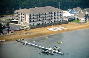 Un hotel de varios pisos con vistas a la playa, un muelle con barcos y una playa de arena con sillas de descanso.