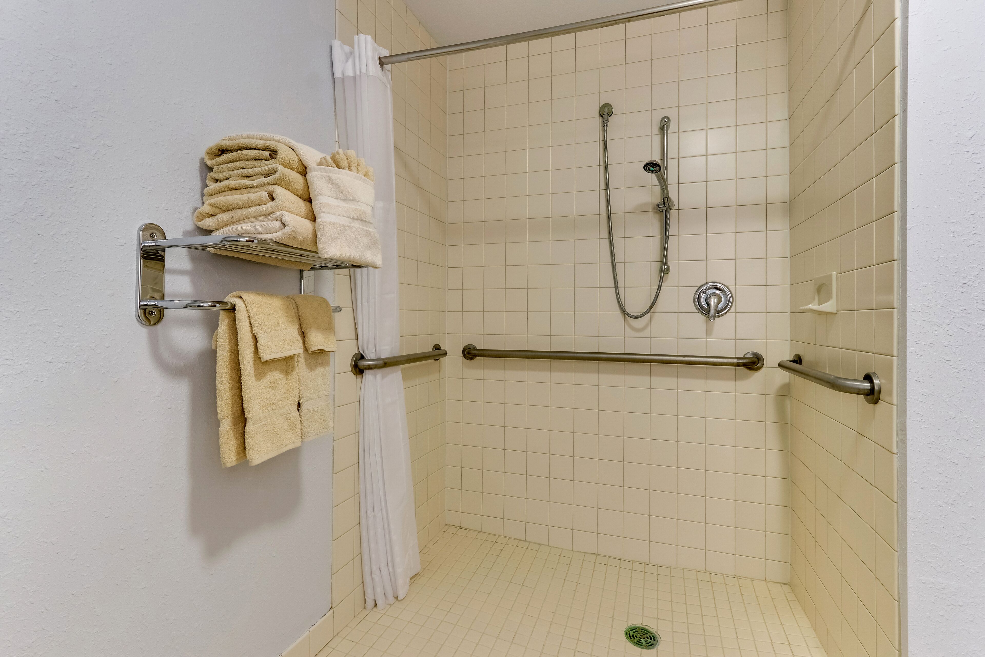 Zona de ducha con barra de apoyo, perchero con toallas dobladas y cabezal de ducha.