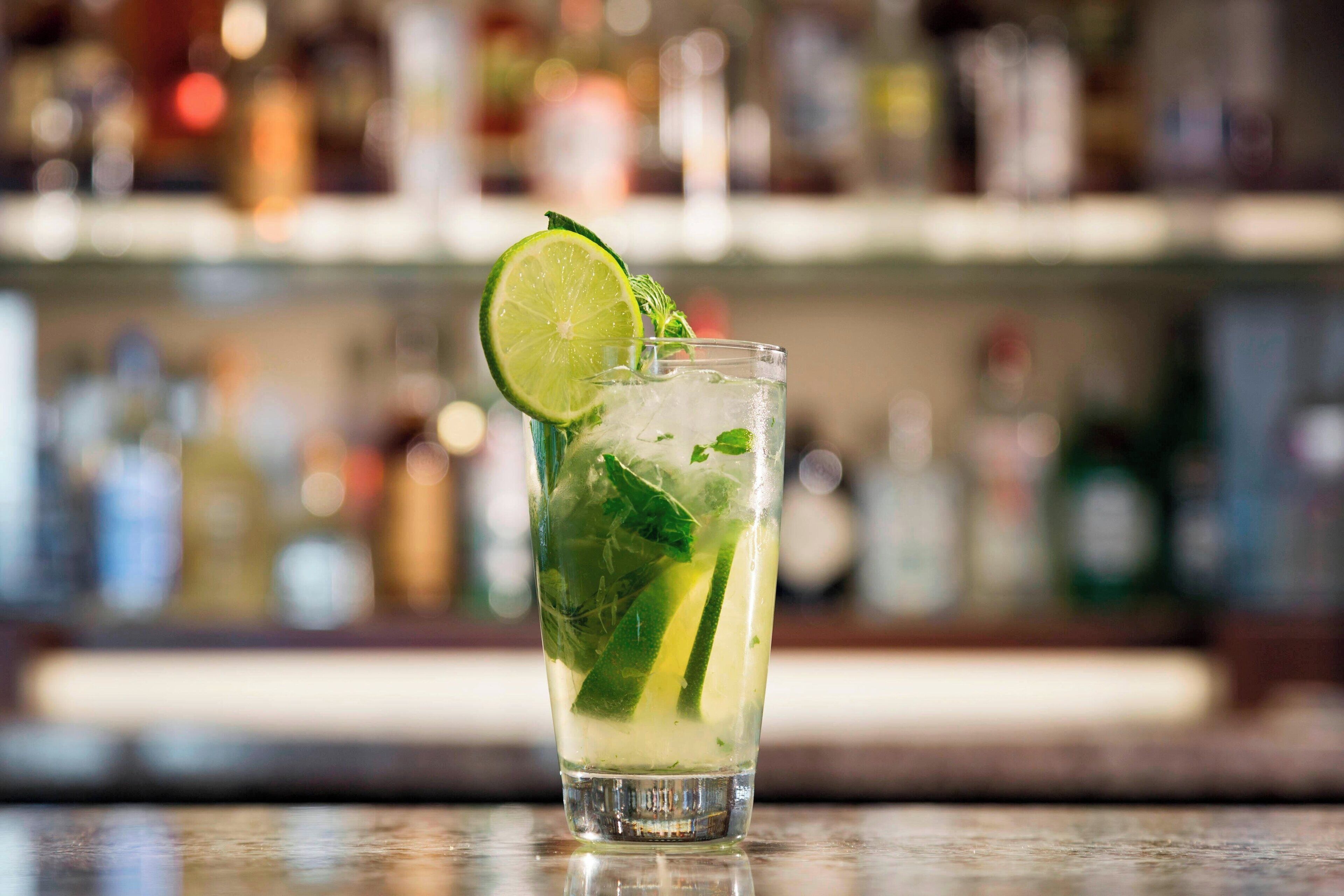 Ett glas med en limebaserad cocktail, garnerad med myntablad och en limeskiva, står på bardisken.