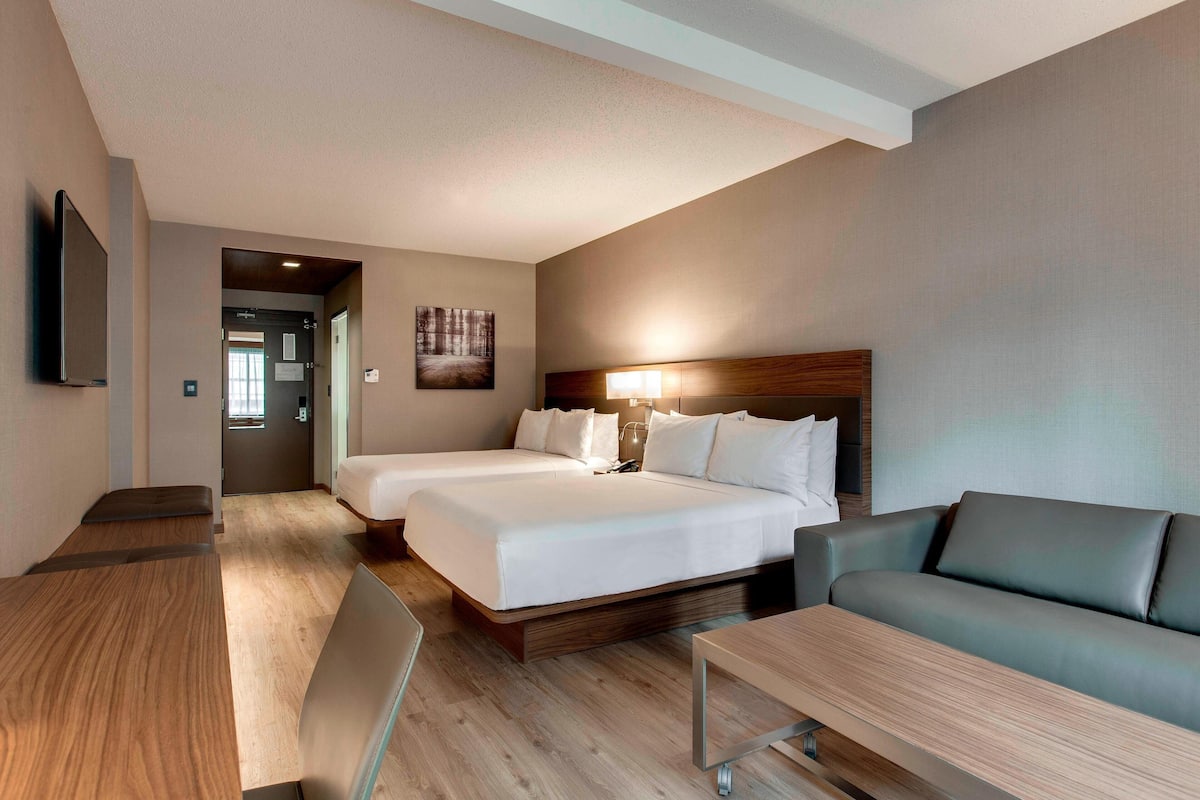 A hotel room with two beds, a sofa, a desk, and a TV.