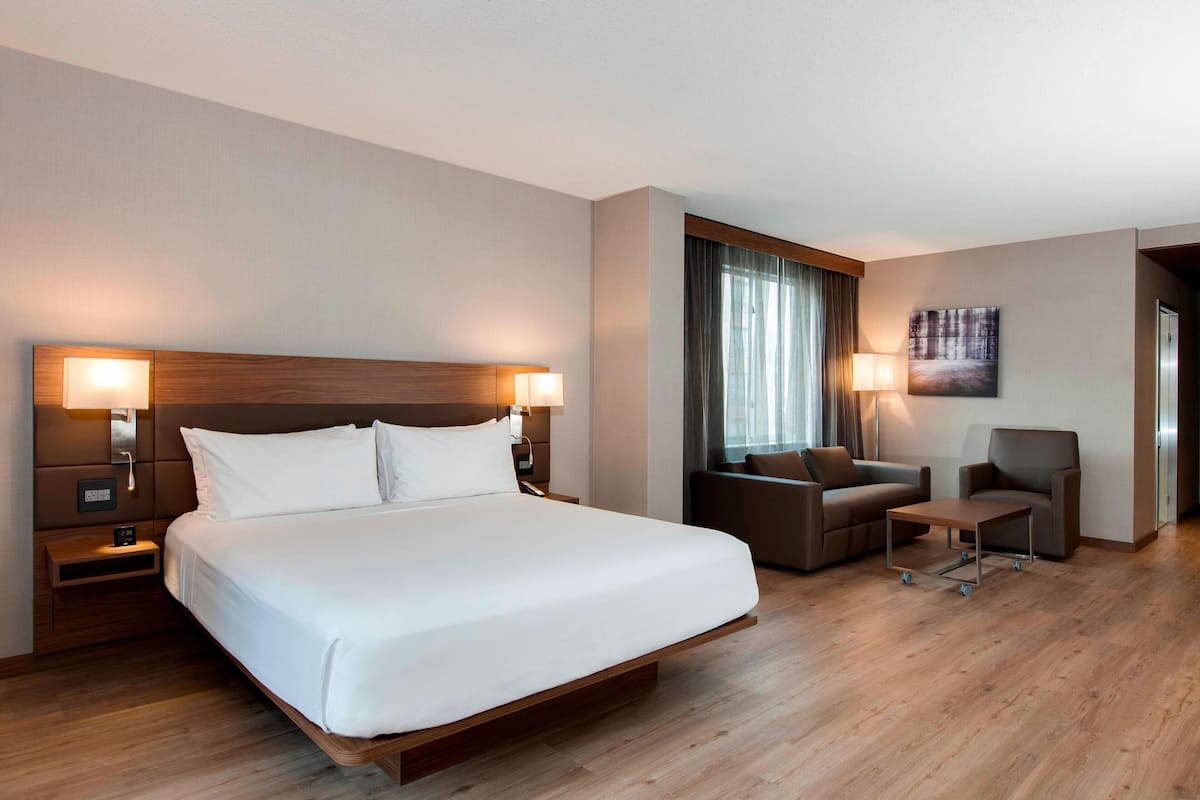 A modern hotel room with a large bed, bedside tables, a desk, and a sofa.