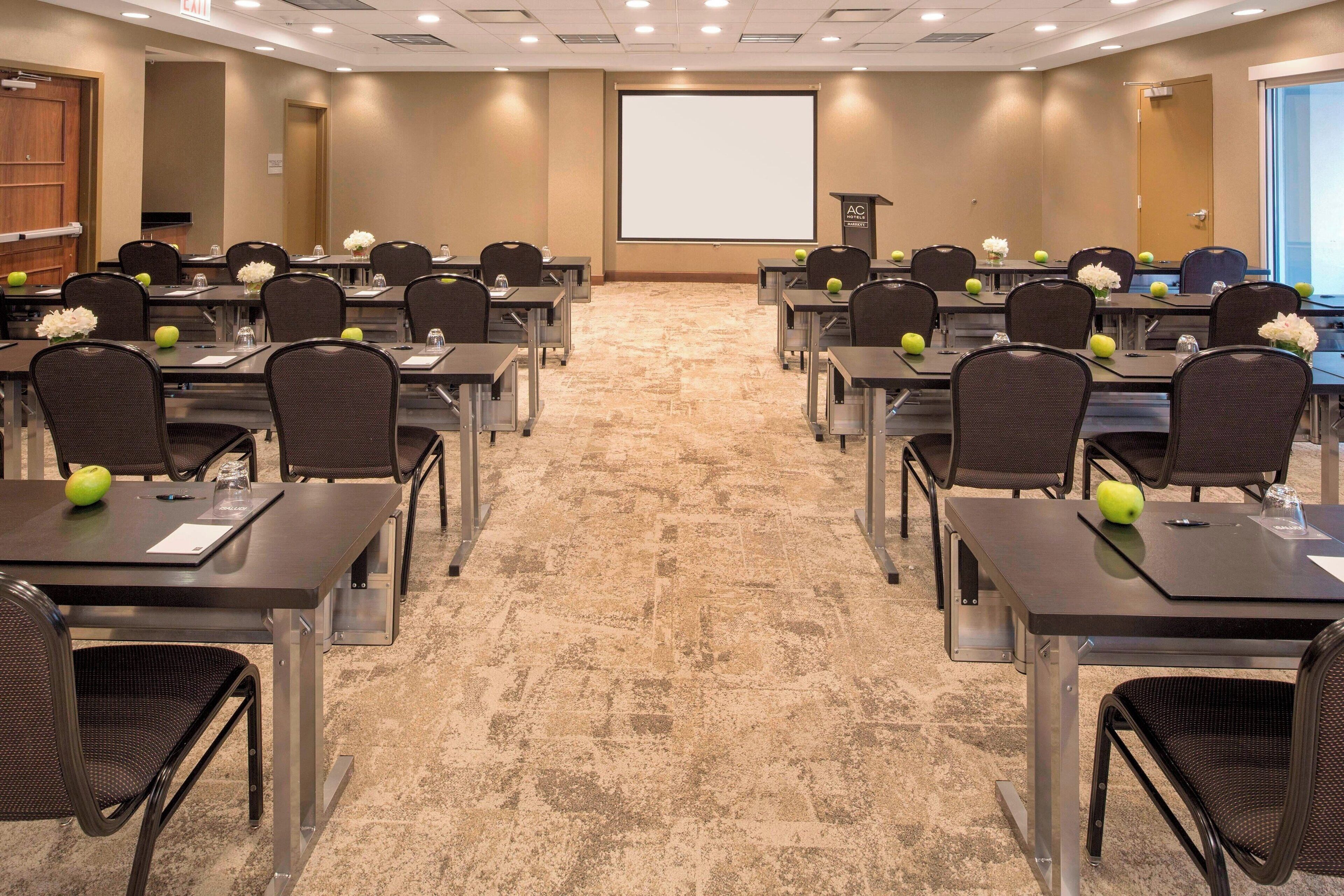A conference room with multiple tables, chairs, and a projector screen.