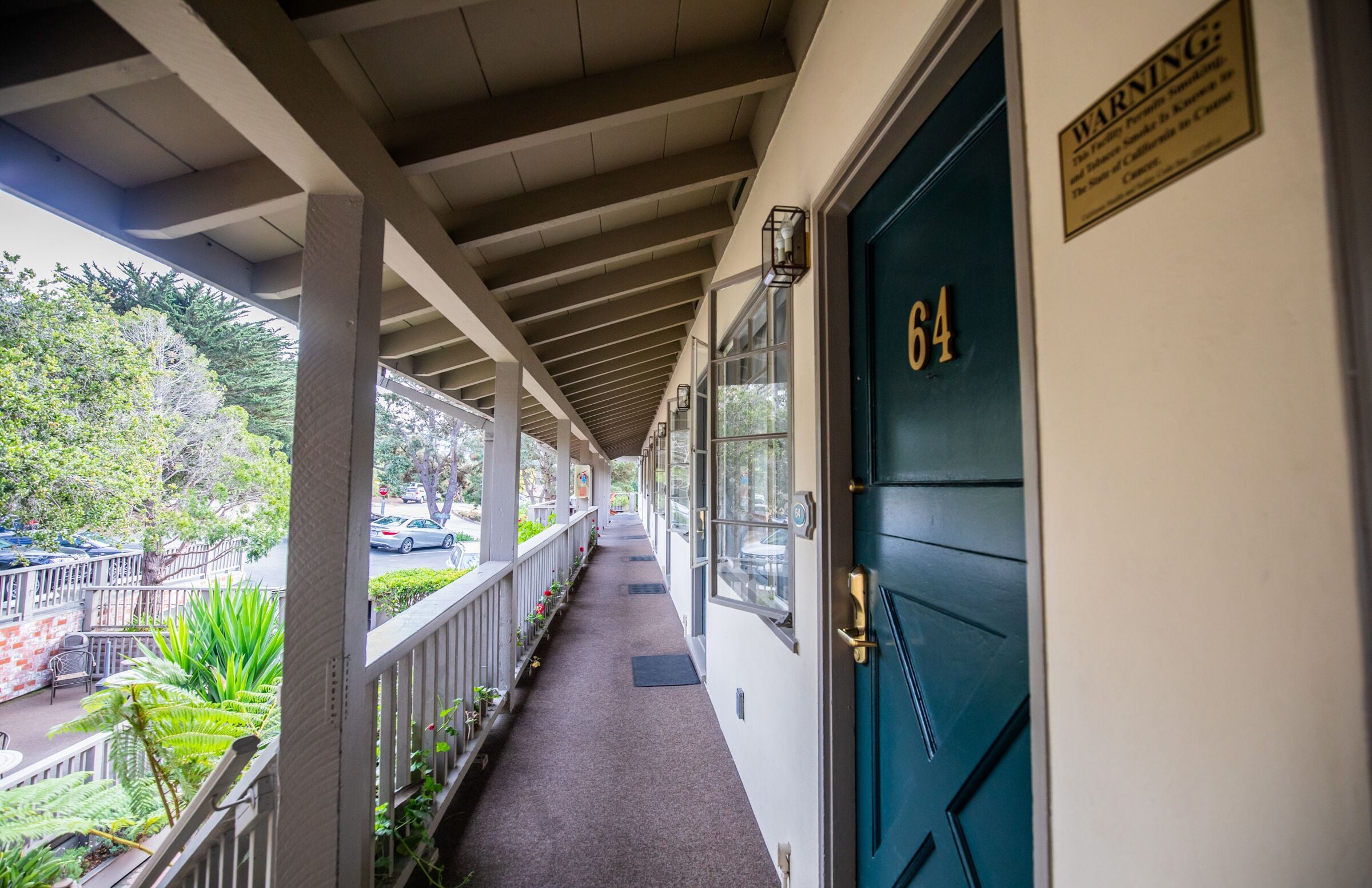 A covered corridor with a blue door marked "64" and a warning sign.