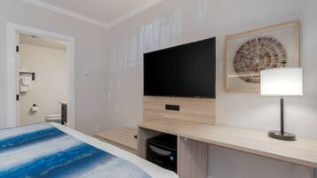 A modern hotel room with a bed, a flat-screen TV mounted on a wooden console, a wall-mounted lamp, and a framed artwork above the console.