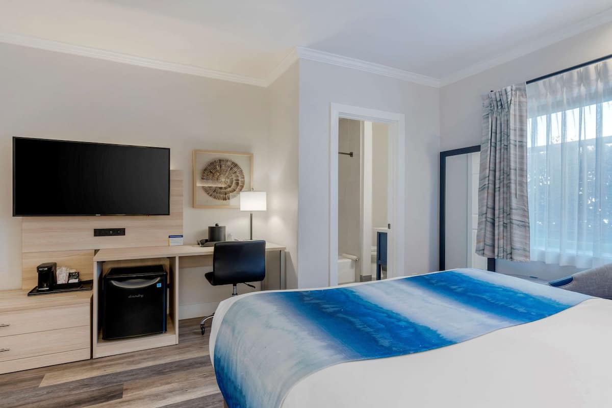 A hotel room with a bed, a TV, a desk with a chair, a coffee machine, and a wardrobe.