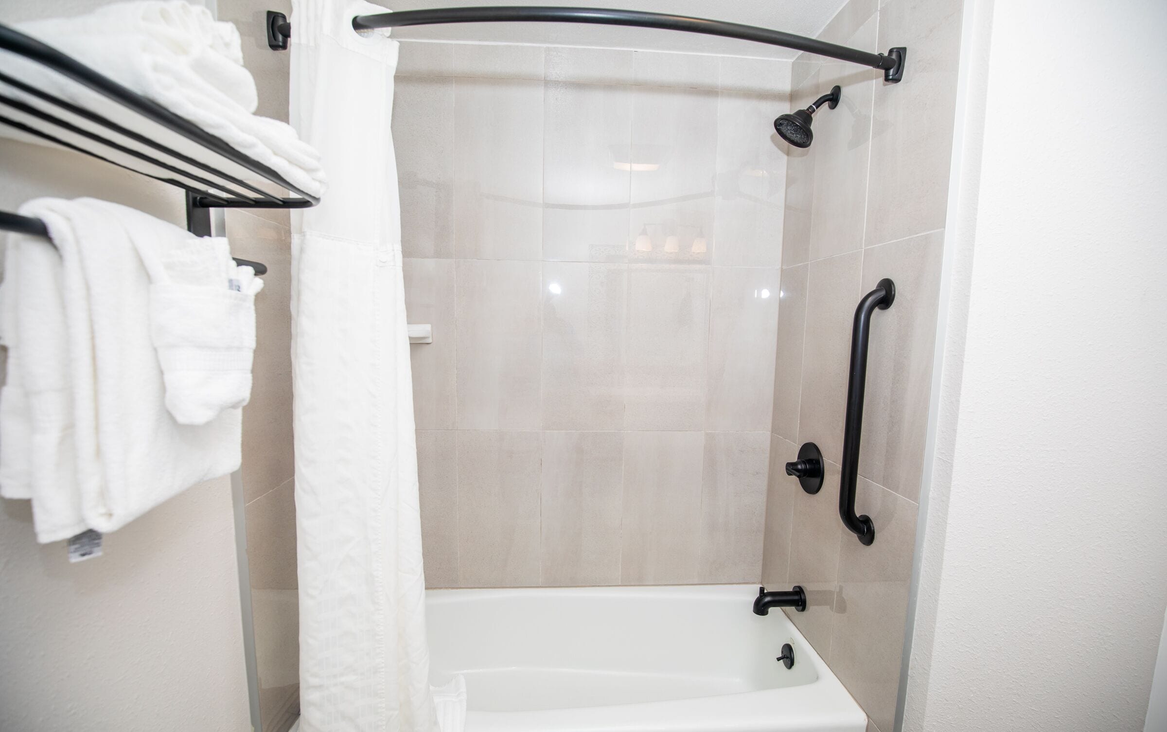 A modern bathroom with a walk-in shower, a white bathtub, and a towel rack with folded towels.