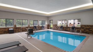Una piscina interior con vistas despejadas al exterior, paredes de piedra y algunas sillas y mesas.