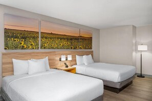 Habitación de hotel con dos camas, un cabecero de madera, una mesita de noche con lámpara y un cuadro grande de un campo de girasoles en la pared.