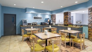 Un restaurante con mesas de madera y sillas amarillas, una zona de cocina y un pilar de piedra.