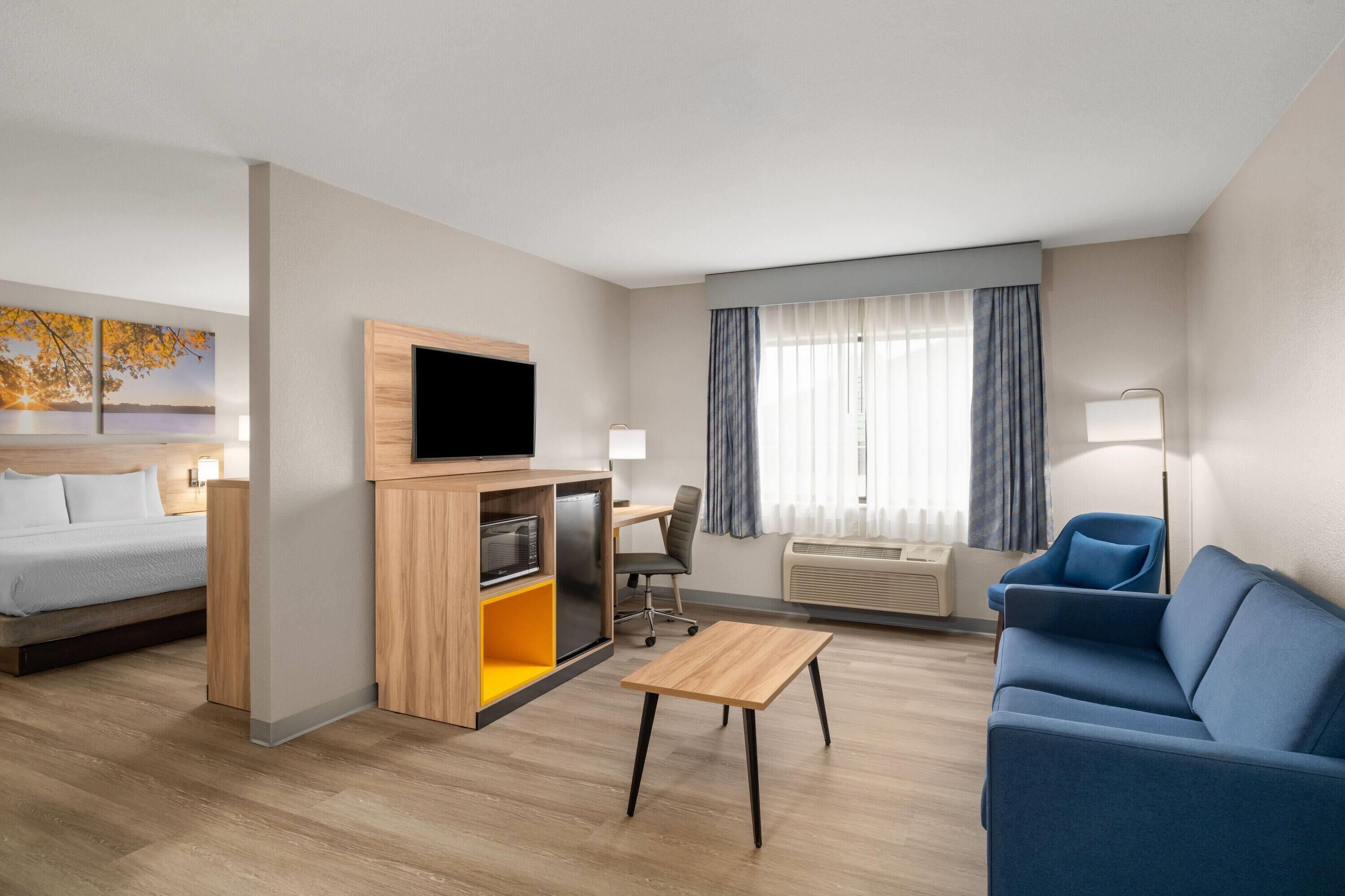 Una habitación de hotel moderna con una cama, un televisor, un escritorio, un sofá azul y una ventana con cortinas.