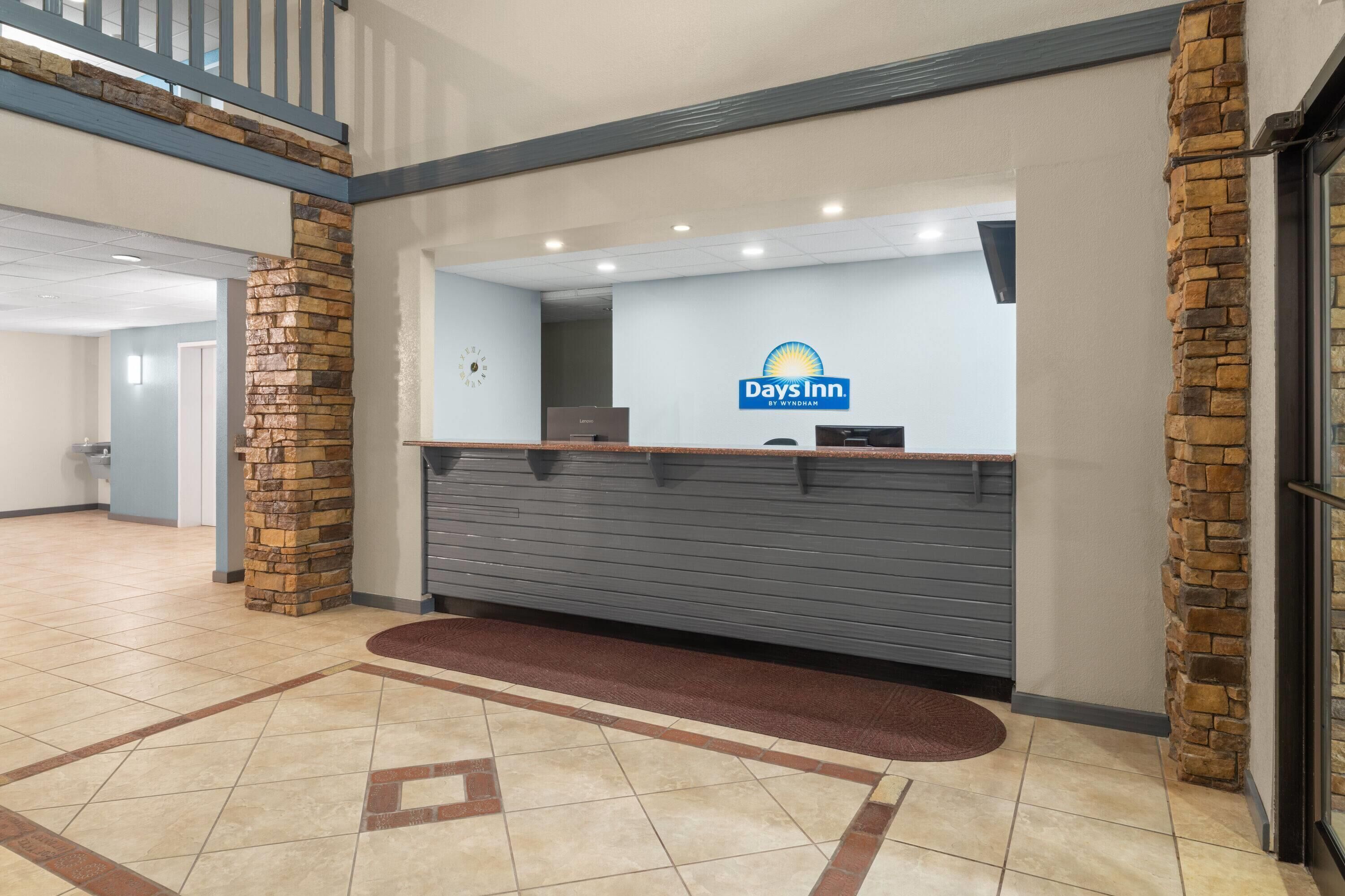 Un espace d’accueil avec un pilier en pierre, un comptoir de réception et le logo de la chaîne Days Inn.