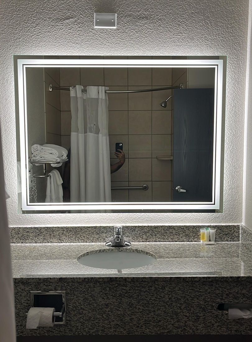 Een badkamer met een grote spiegel, een wastafel, een handdoekrek en een douchegordijn.