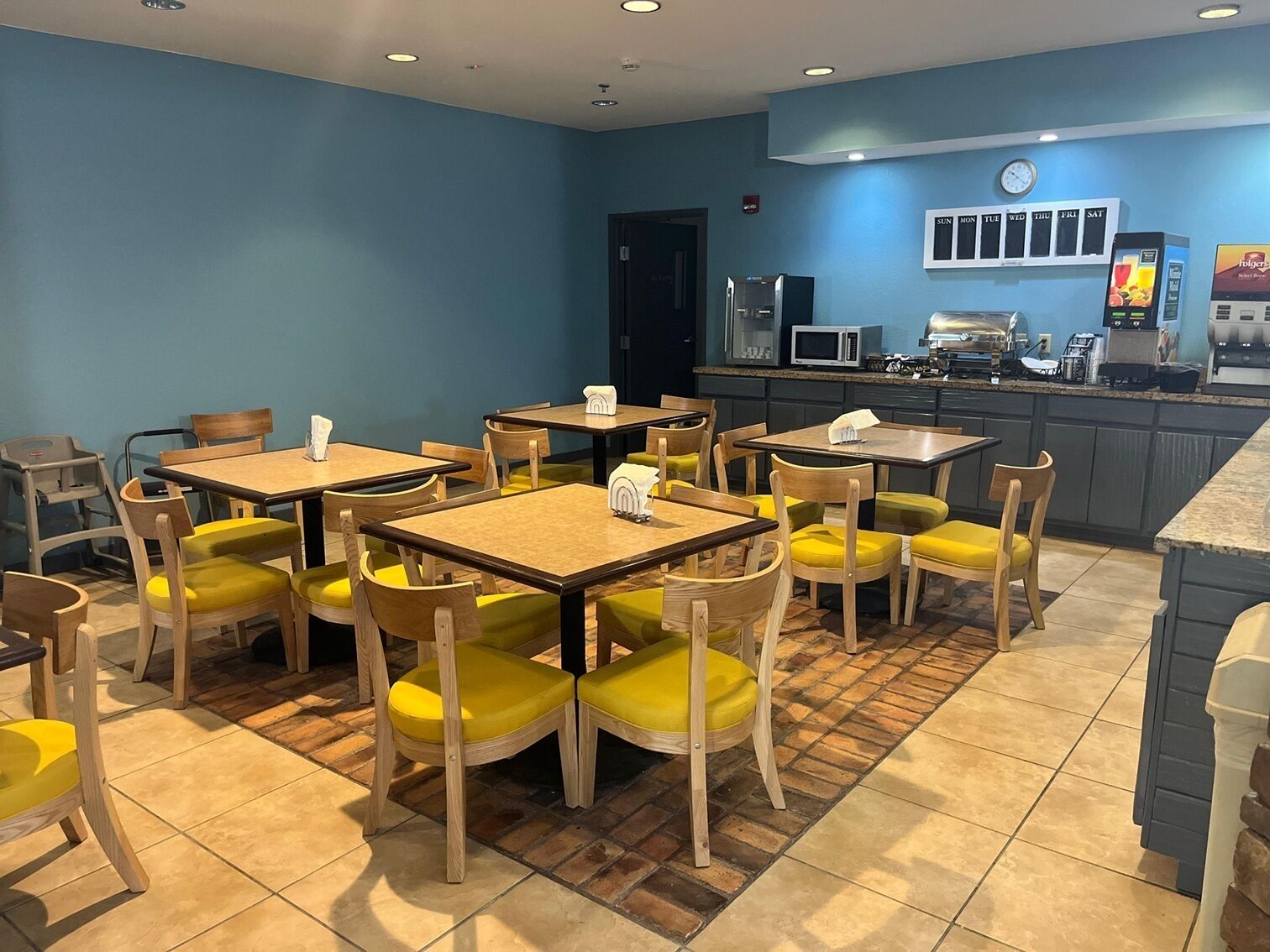 A restaurant with multiple tables and chairs, a kitchen area, and a clock on the wall.