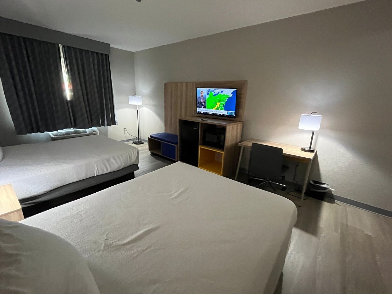 A hotel room with two beds, a TV on the wall, a desk, and a chair.
