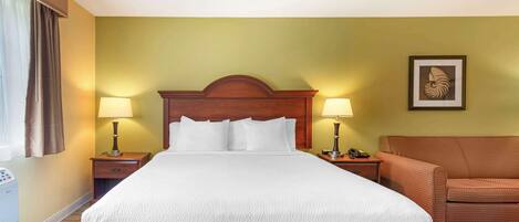 A hotel room with a large bed, two bedside tables with lamps, a brown upholstered chair, and a framed picture on the wall.