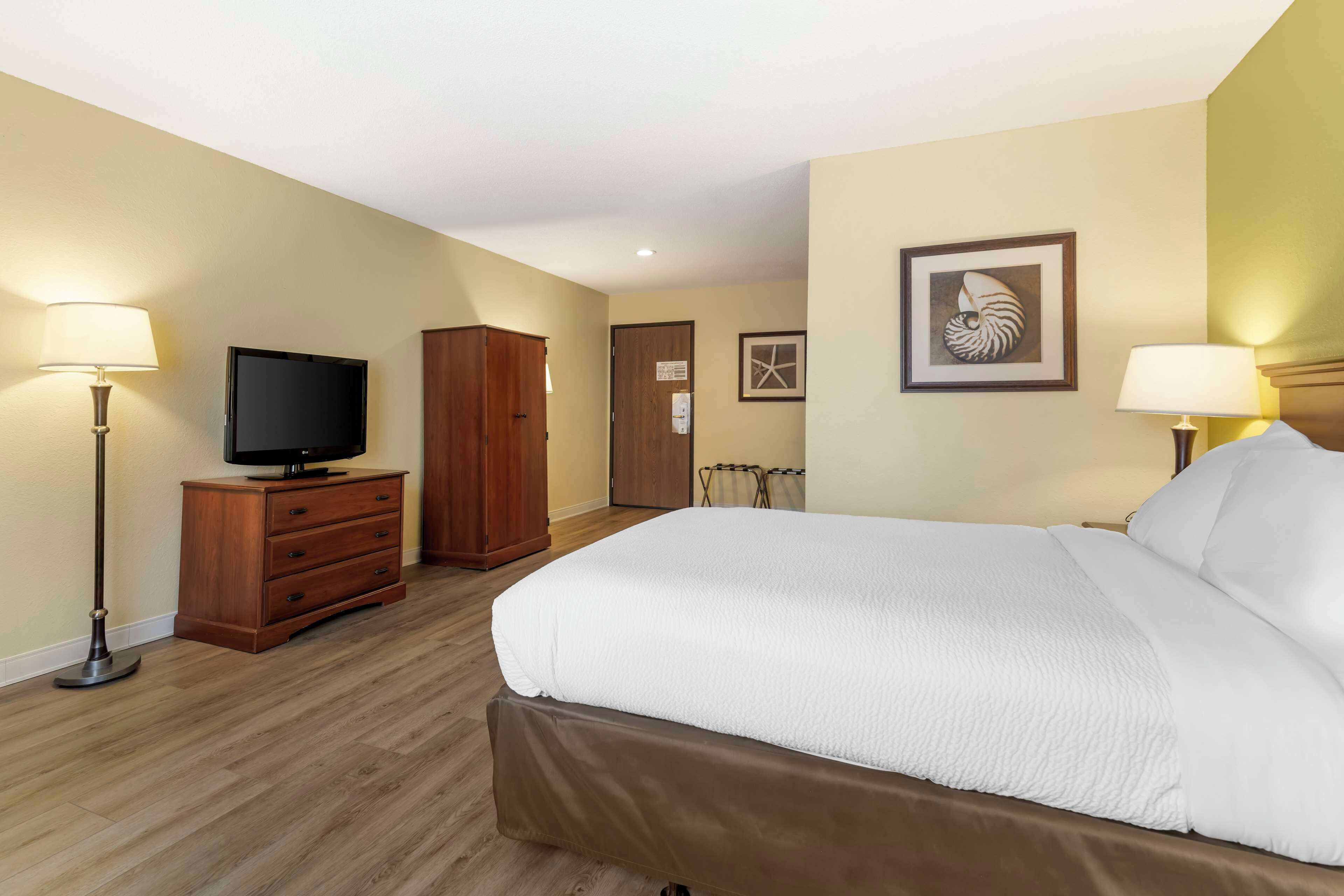 A hotel room with a large bed, a wooden dresser, a television, and two lamps.
