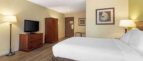 A hotel room with a large bed, a wooden dresser, a television, and two lamps.