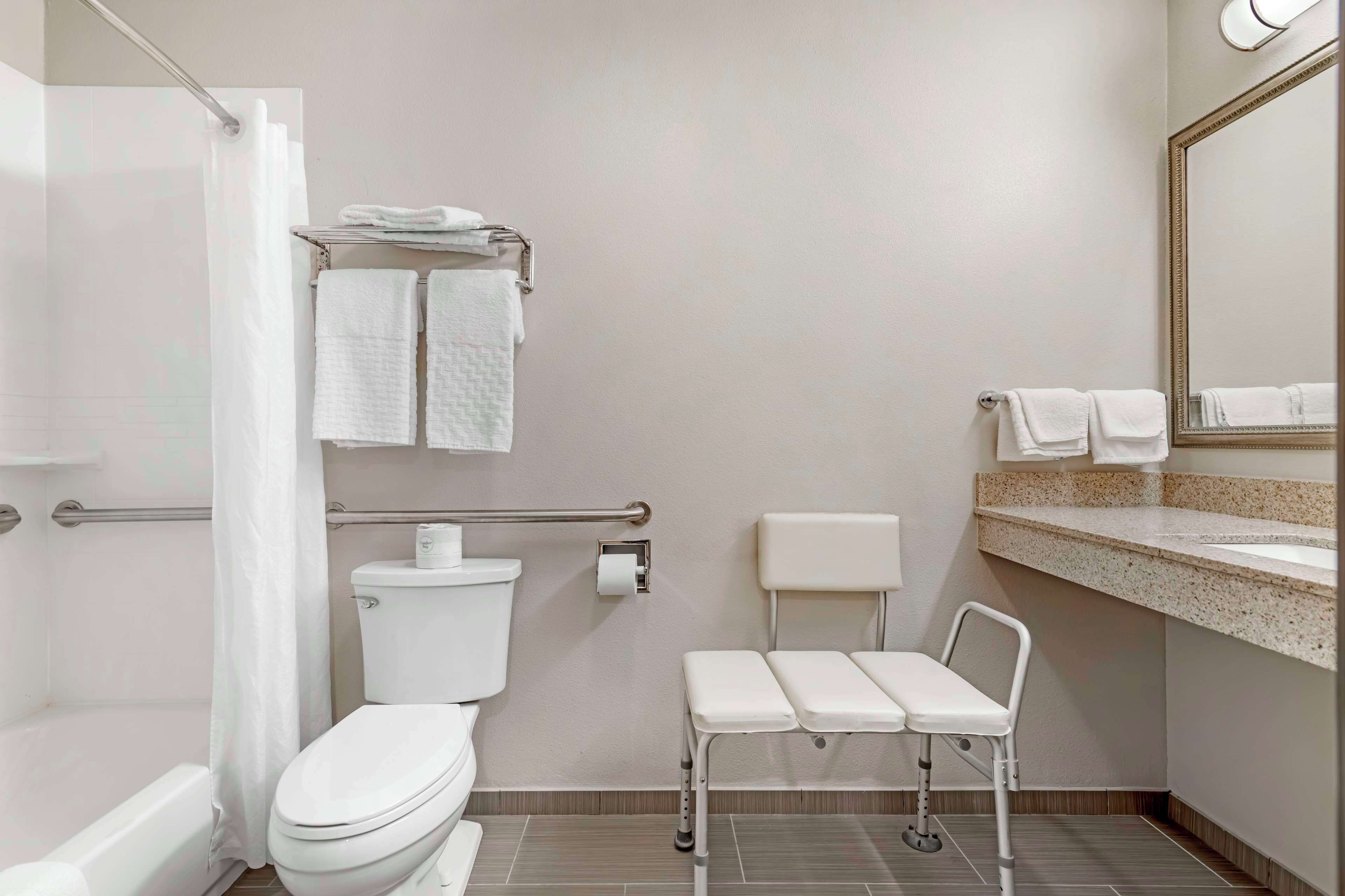 A modern bathroom with a toilet, a shower, a sink with a mirror, and a bench.