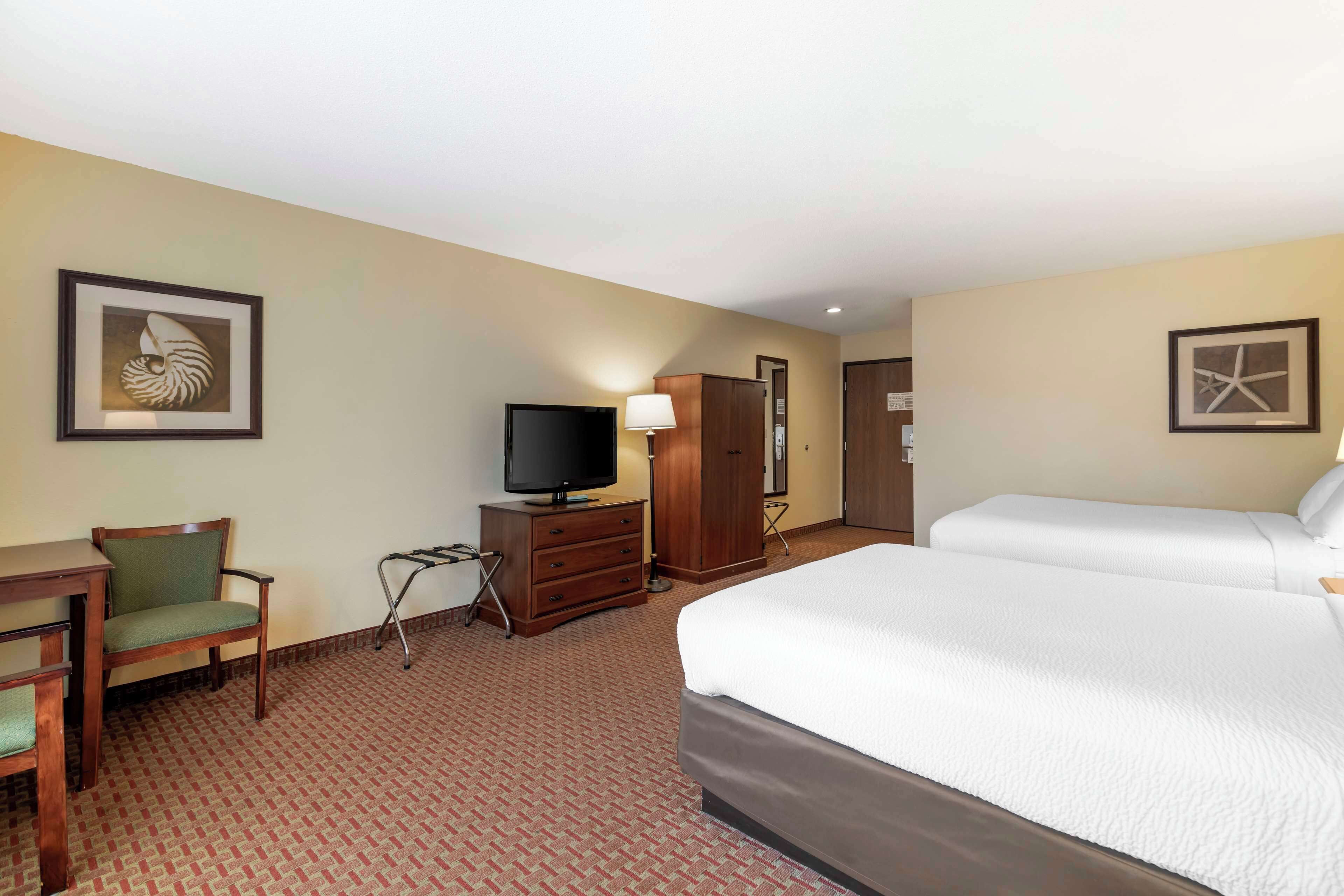 A hotel room with a bed, a desk with a chair, a television, a wardrobe, and two framed pictures on the walls.