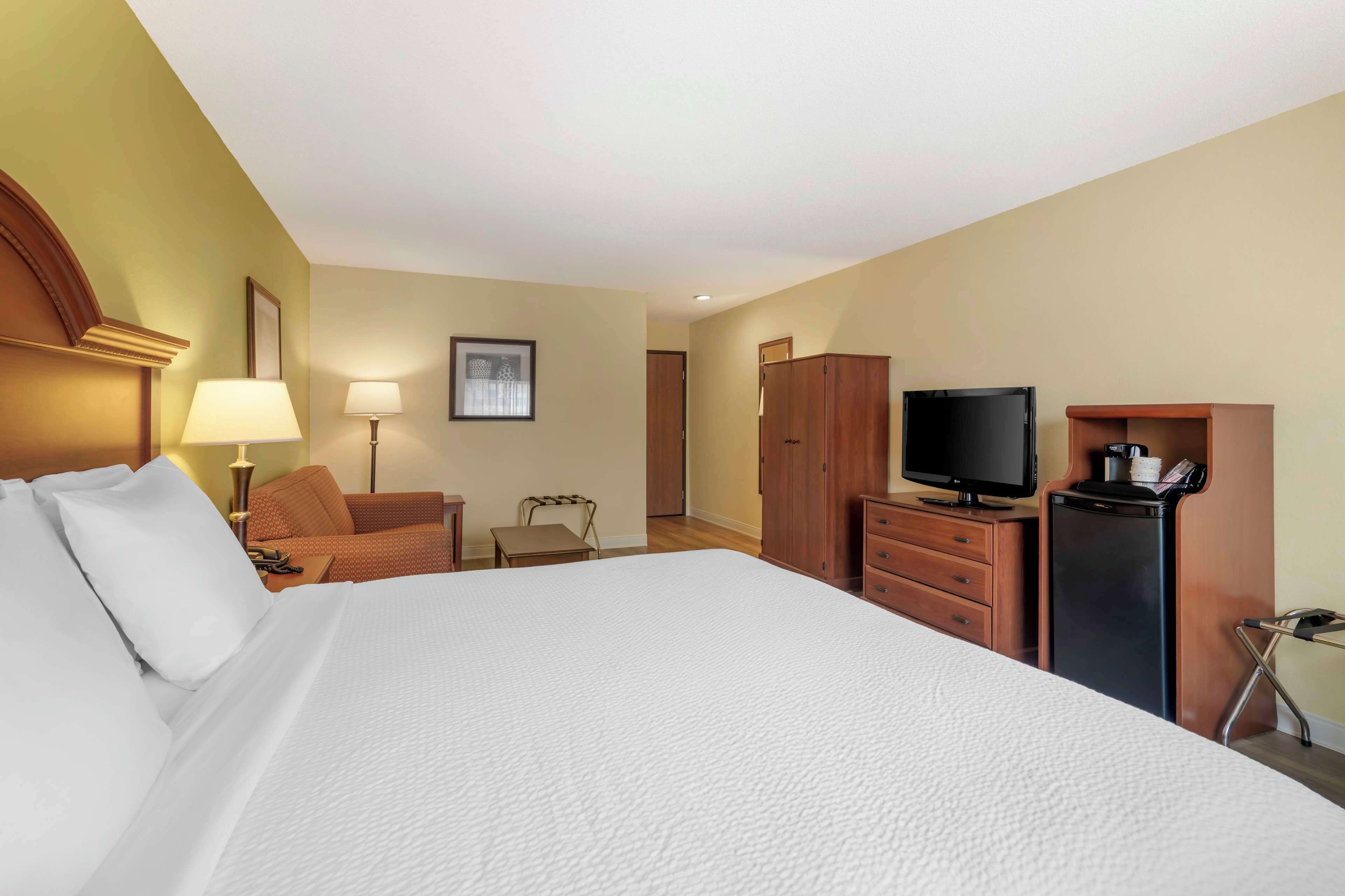 A hotel room with a large bed, a desk with a computer, a TV, and a small refrigerator.