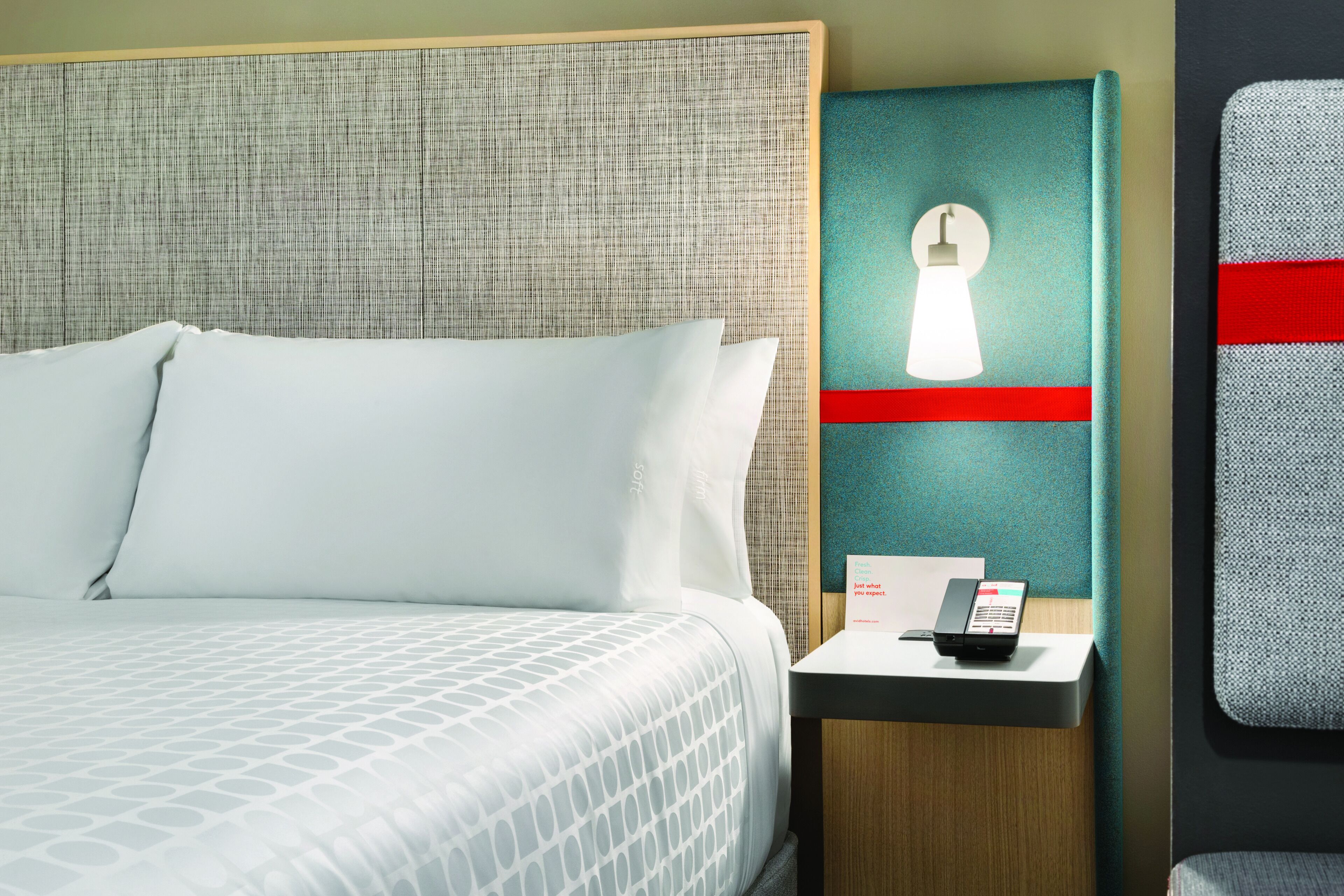 A hotel room with a bed, a nightstand with a phone, and a wall-mounted light fixture.