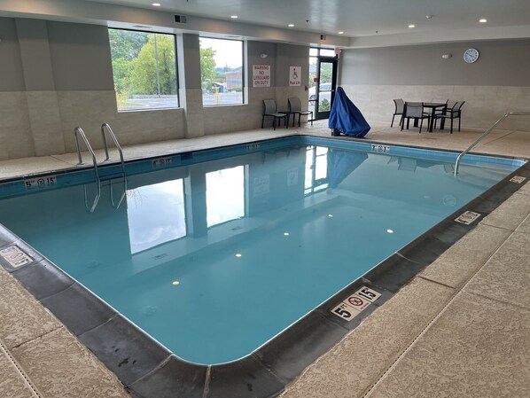 An indoor swimming pool with clear water, safety signs, and a lifeguard chair.