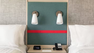 Une chambre d’hôtel avec deux lits, une table de chevet dotée d’une horloge numérique, un téléphone et deux lampes fixées au mur.
