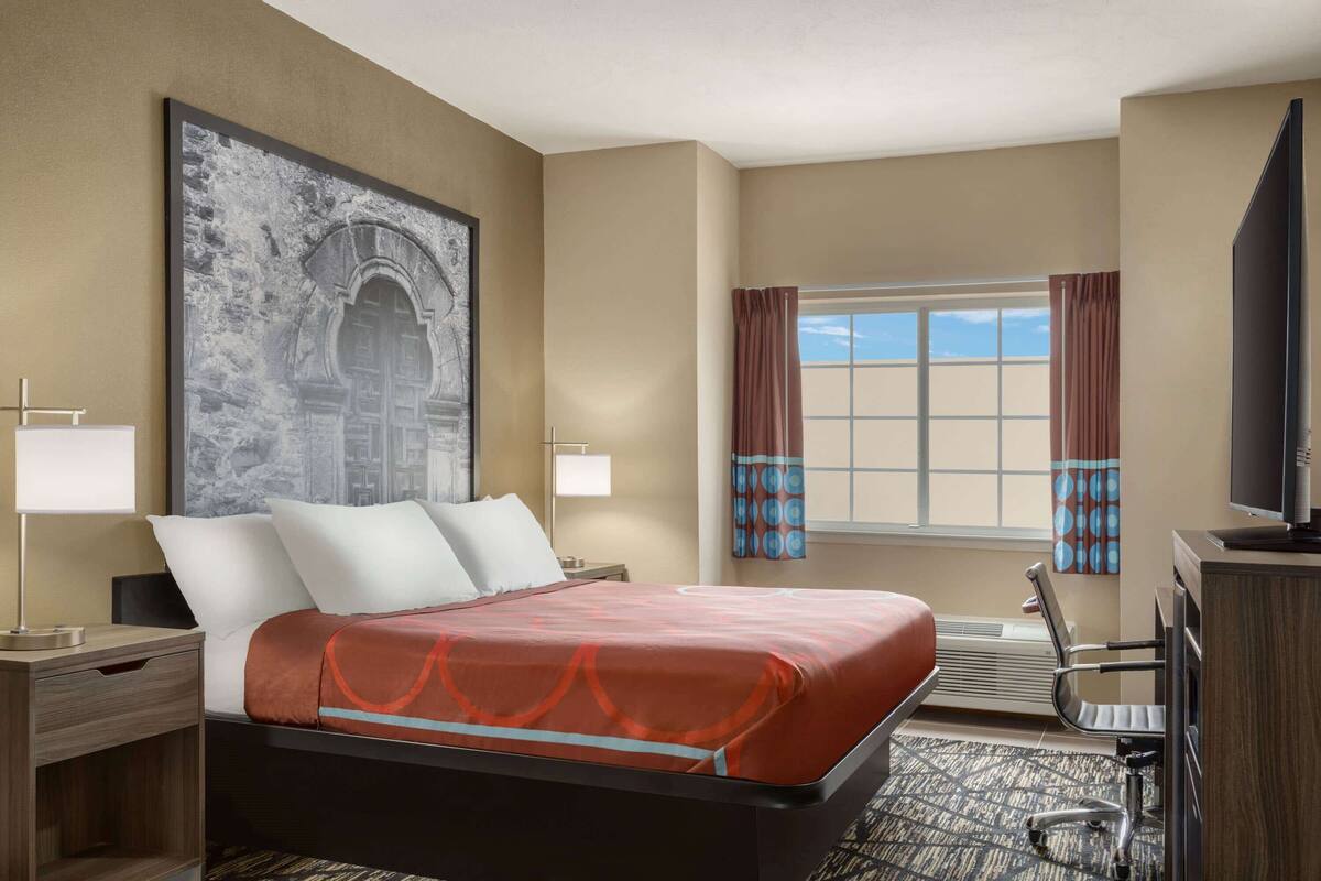 Une chambre d’hôtel avec un lit, un bureau, une télévision et une grande fenêtre avec des rideaux.