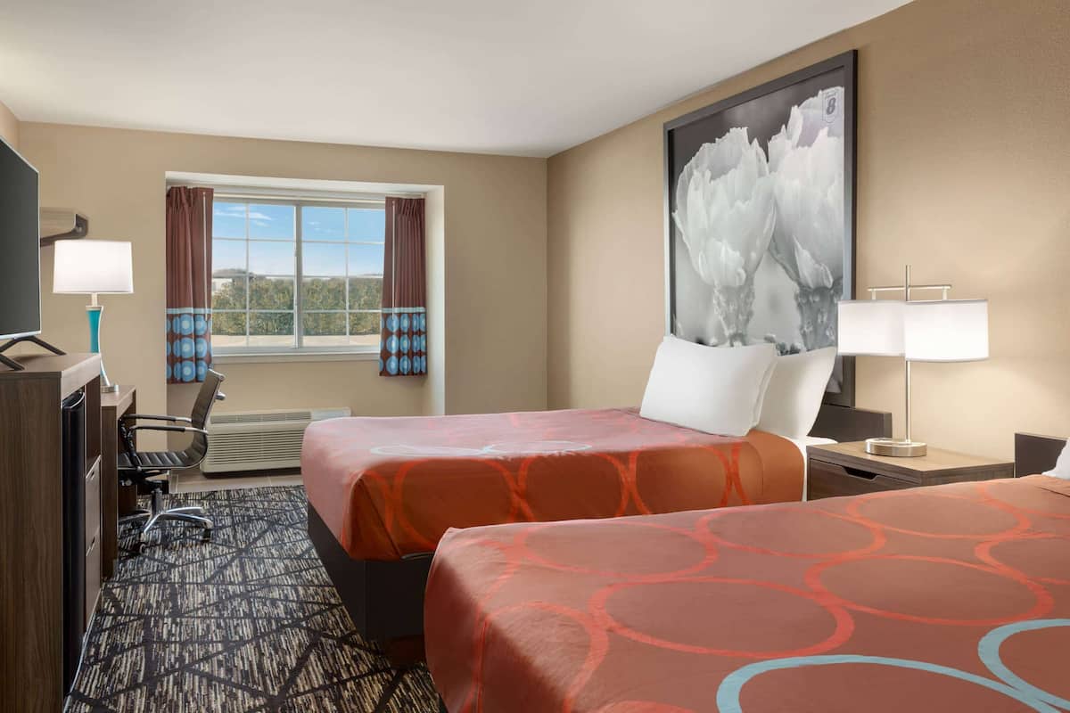 Une chambre d’hôtel avec deux lits, un bureau avec une chaise, une grande fenêtre avec des rideaux et un tableau au mur.